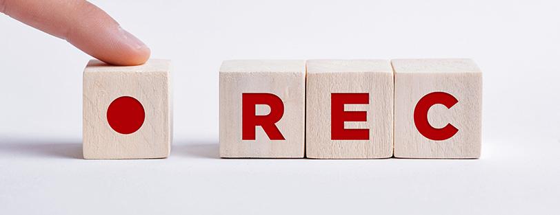 Svenska: Ett finger trycker på en träkub med en röd inspelningssymbol bredvid tre träkuber med bokstäverna ”REC”.