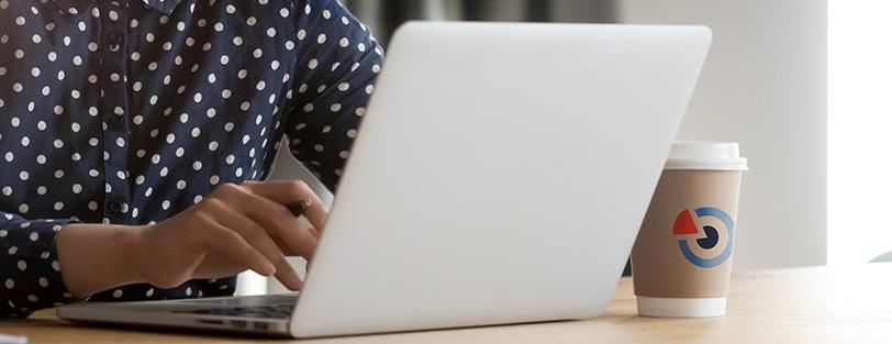 Person vid laptop, en kaffekopp med SND-logotyp står på skrivbordet.