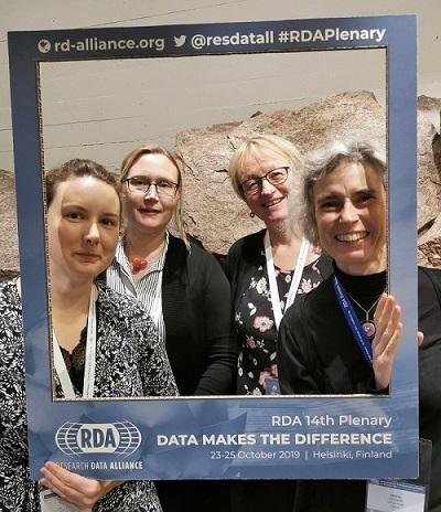 Photo of four conference participants who hold a large frame with printed text about the RDA meeting in Helsinki in 2019.